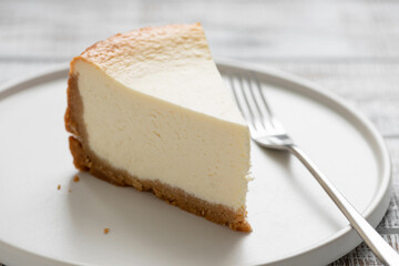 A decent slice of new york style cheesecake on a white plate, closeup view