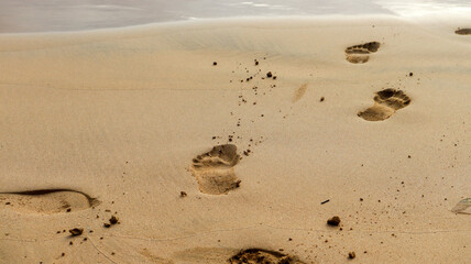 Marcas de pegadas humanas na areia de praia tropical em Noronha, Brasil. Representa turismo, descanso e harmonia com a natureza em cenário paradisíaco
