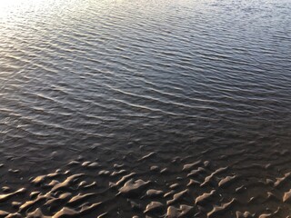 sunset gray beach wavy sand ripples water ocean or sea dune texture wallpaper pattern background close-up	