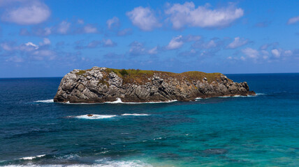 Ilha rochosa isolada cercada por mar azul vibrante em dia ensolarado, destacando natureza selvagem e oceano cristalino em cenário tropical impressionante