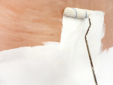 Close up virew of a paint roller being used to coat bare plaster with white primer paint