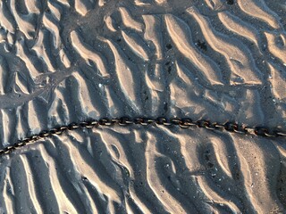Textured beach sand with a metal chain tidal ripples texture background