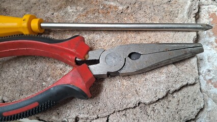 Close-up of a screwdriver and pliers on a brick surface
