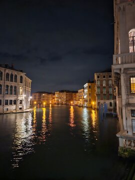 Venice canal at night with reflections of lights on the water and historic Venetian buildings under cloudy sky