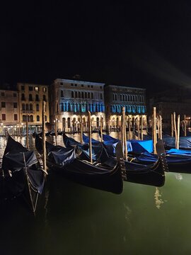 Venice blue gondolas at night with historic illuminated buildings along the Grand Canal in Italy
