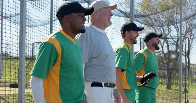 Celebrating successful play, diverse teammates wearing uniforms clapping gloves at fence for team