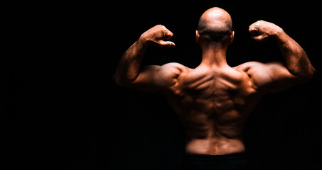 Muscular man with arms raised viewed from behind in dramatic light on black background