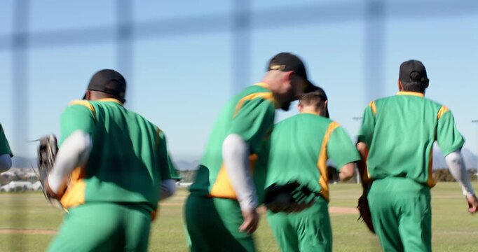 Executing fist bump near fence, five male baseball players jogging toward outfield for defense