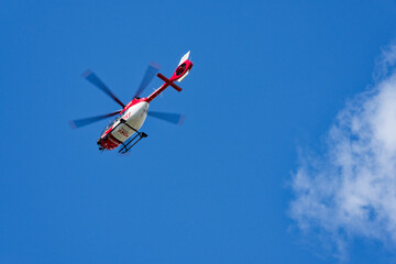 Red and white rescue helicopter flying in blue sky in Flensburg