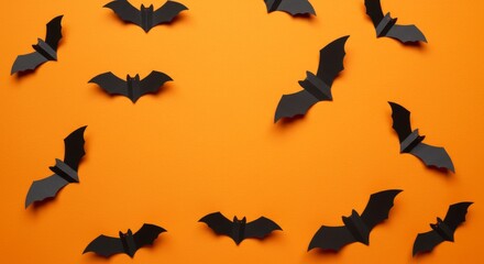Halloween flat lay with black paper bats decoration on vibrant orange background in minimalist top-down design