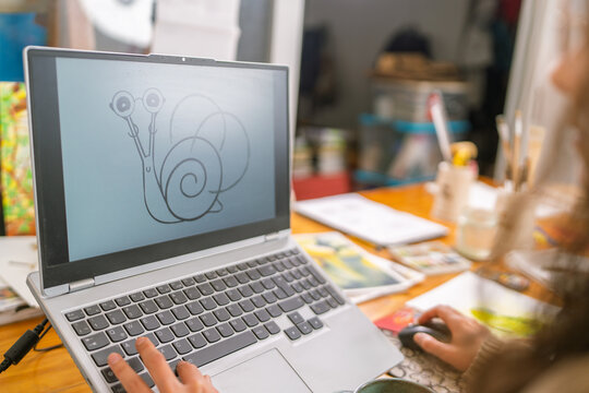 Graphic designer creating funny snail character on laptop in home studio