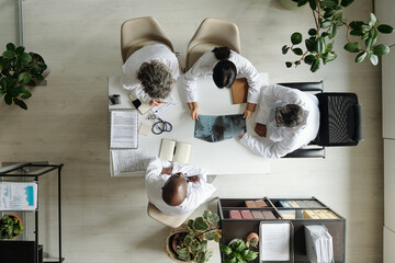 Group of middle aged and senior multiethnic doctors sitting around table discussing medical images and patient charts, collaborating on diagnosis and treatment plan in clinical setting