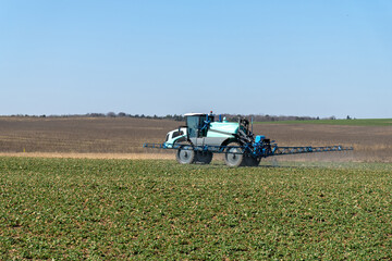 Fototapeta premium Blue wheel tractor spraying liquid fertilizer on a field during springtime.