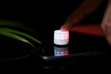 Finger pressing a small illuminated device on a dark surface