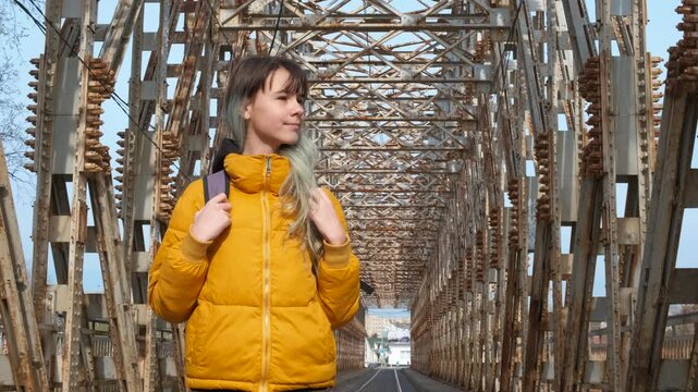 Teen on bridge with metal structures. A view of happy hopefull teen girl stand on metal rusty bridge