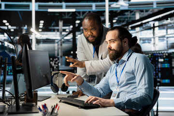 Team of system administrators using computer in server farm, analyzing data. Data center office colleagues doing brainstorming, examining equipment, ensuring system integrity and security