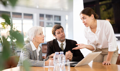 Adult man, elderly woman and young woman in business clothes having meeting in office