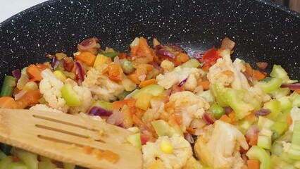 A woman fries vegetables in a frying pan at home. healthy food, diet, low calories, diet. cauliflower, green beans, peas, peppers, tomatoes. Vegetable saute in frying pan