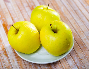 Juicy golden delicious apples are on plate. Yellow fruits shine in rays of sun and lighting