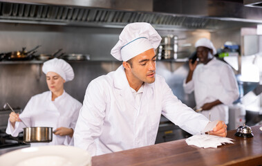 Portrait of focused man chef working in restaurant kitchen, checking orders on order station