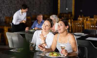 Young woman and adult woman have dinner and drink wine together in restaurant