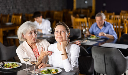 Young girl having lunch at restaurant talking with elderly friend mom. Sad upset young woman shares with mature female friend talks about difficulties of interpersonal communication in team at work.