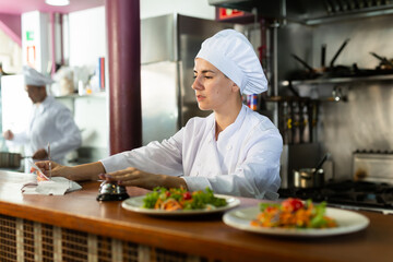 Female cook reads the paid check and presses the bell for the waiter in the restaurant