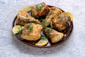 Fried fish pieces on plate with dill and lemon slices. Delicious seafood meal for dinner. Grilled healthy food serving from top view on concrete background.
