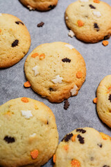 Halloween cookies with orange glitter sprinkles in shape of pumpkin, Sugar cookies with spooky funfetti ghosts bats decoration on baking sheet, freshly baked golden homemade sugar and butter biscuits