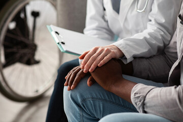Bad news, health problems, trauma, rehab with nurse at home. Young lady doctor in white coat calms adult african american patient in living room or clinic interior with wheelchair, cropped, free space