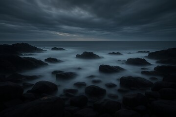 Fototapeta premium Moody seascape with dark rocks and misty water under dramatic, stormy skies