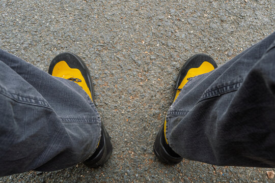A person is standing on a sidewalk with their feet apart