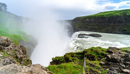 Fototapeta premium Majestic waterfall cascades down a rugged cliff face, shrouded in a misty spray, showcasing Iceland's dramatic landscape.