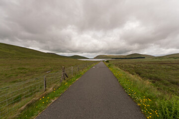 A road with a fence on the side and a lake in the background