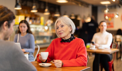 Elderly woman meets a man in a cafe. Conversation over a cup of coffee