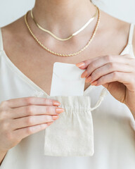 Woman taking necklace jewelry card out of linen woven sachet bag wearing gold necklaces