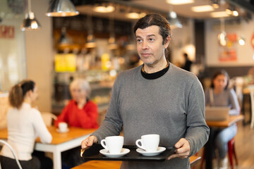 Breakfast in cafe - man carries tray with two cups of coffee