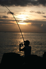 Silhouette of fisherman holding rod at sea sunset