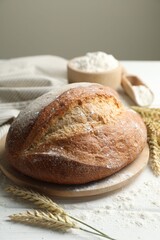 Loaf of fresh bread, flour and spikes on white wooden table, closeup