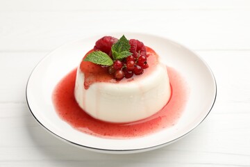 Delicious panna cotta with berries, sauce and mint on white wooden table, closeup