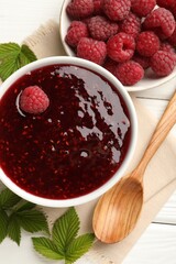 Sweet raspberry jam in bowl and berries on white wooden table, flat lay