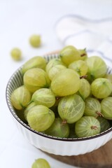 Fresh green gooseberries in bowl on white table, closeup