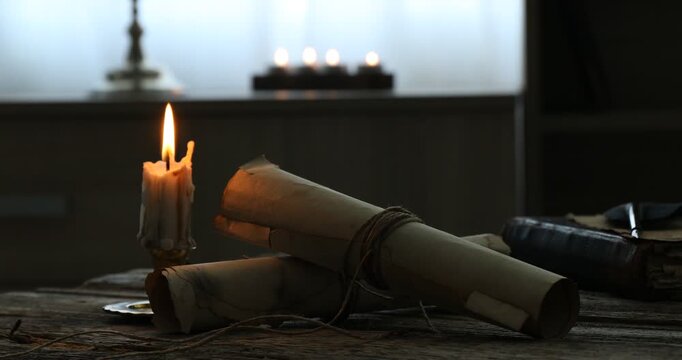 Old rolled scrolls and burning candle on wooden table, closeup