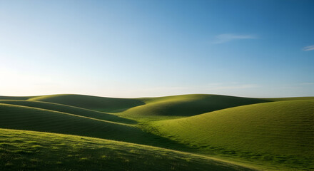 Obraz premium Scenic landscape of rolling green hills under a clear blue sky with gentle sunlight creating a peaceful and natural outdoor scene perfect for nature and travel themes