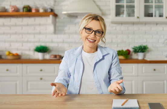 A young woman wearing casual clothes looking at camera having video call sitting at the desk at home. Satisfied confident girl chatting online or having video conference in kitchen. - Powered by Adobe
