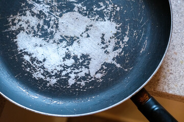 Old frying pan with damaged non-stick coating and scratched surface placed on kitchen countertop