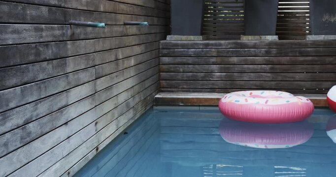 pink donut float floating in backyard pool, featuring beach ball, pool noodles and stacked towels