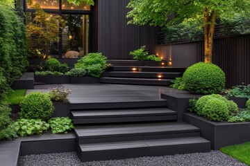 Modern outdoor space featuring dark grey composite decking stairs and platforms, tiered landscaping with lush green shrubs and bushes, 