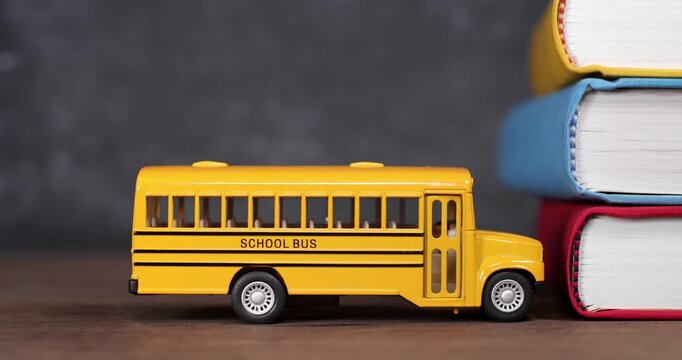 Toy yellow schoolbus driving into school books in front of chalkboard. Classic American public school bus traveling quickly towards school textbooks indicating excitement at going back to school.