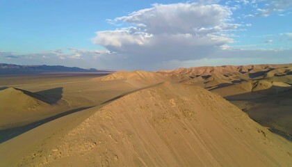 Expansive desert landscape showcases rolling sand dunes under a partly cloudy sky.